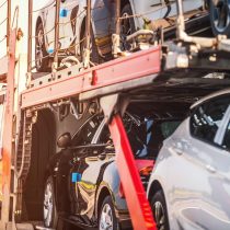 New Delivery to Car Dealer Park. Semi Truck Fully Loaded with Hatchback Vehicles on the Road. Heavy Duty Transit Theme.